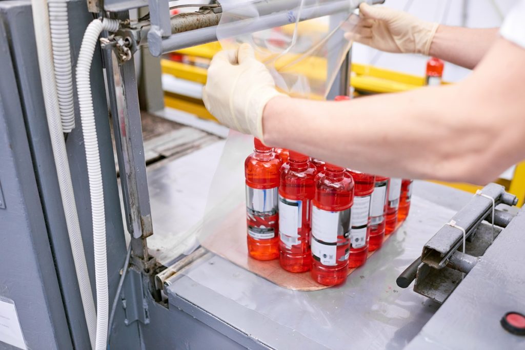 Factory worker packing full bottles into plastic film