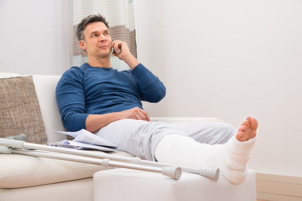 A man on the phone sitting at home with an injured leg